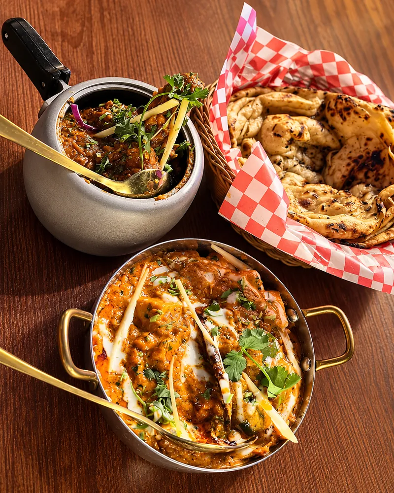Handi chicken in a brass bowl with a curry pot and a basket of naan